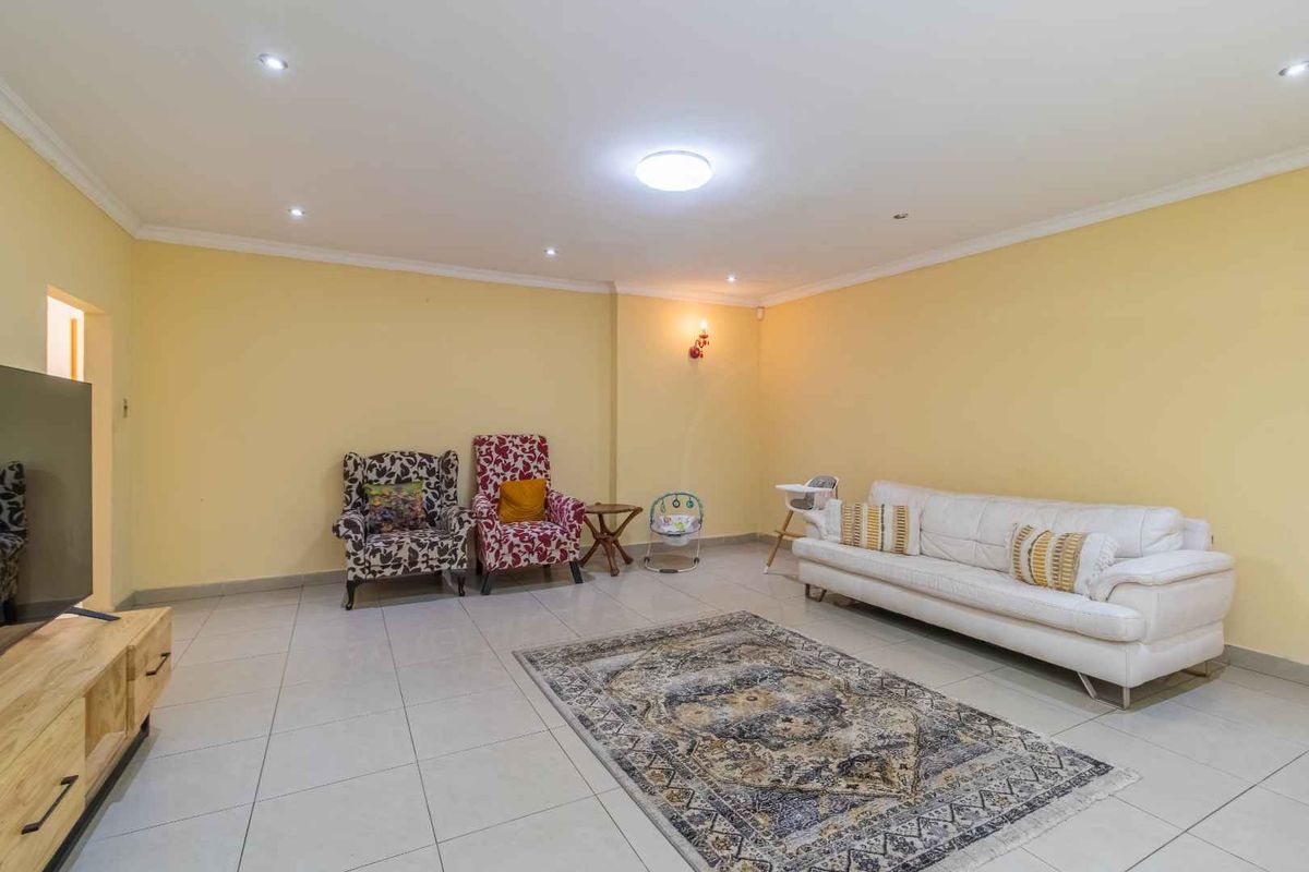 A spacious living room featuring neutral tiled flooring, recessed downlighting, and coved cornicing, providing a versatile area for relaxation and family gatherings.