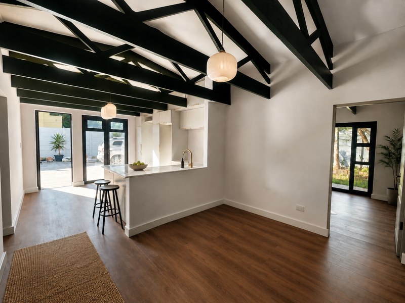 Modern open-plan living and kitchen area featuring high exposed timber beams, sleek cabinetry, stone island countertop, and warm laminate flooring with abundant natural light.