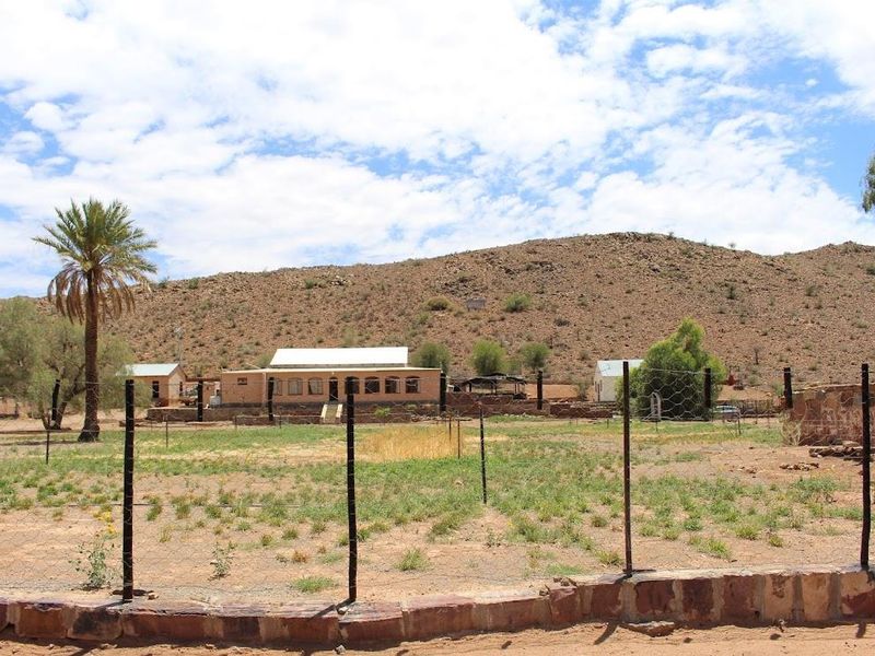 A wide-angle view of a rural farm property featuring a main dwelling, outbuildings, and expansive arid landscape set against a mountain backdrop.