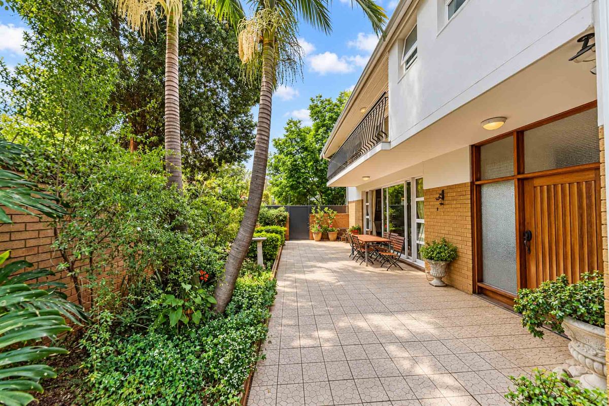 A well-maintained rear patio area featuring tiled flooring, brick exterior walls, and access to a lush, landscaped garden.