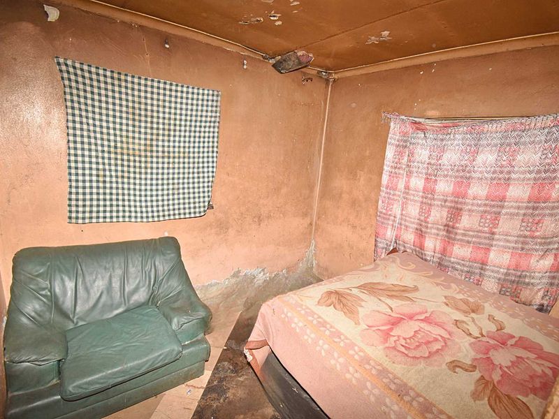 A bedroom space requiring significant renovation, featuring worn wall and ceiling finishes and damaged flooring.