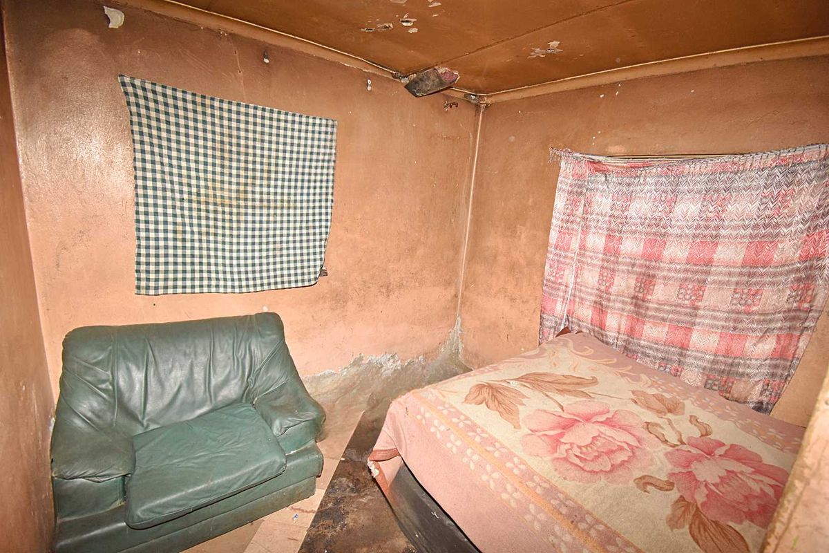 A bedroom space requiring significant renovation, featuring worn wall and ceiling finishes and damaged flooring.