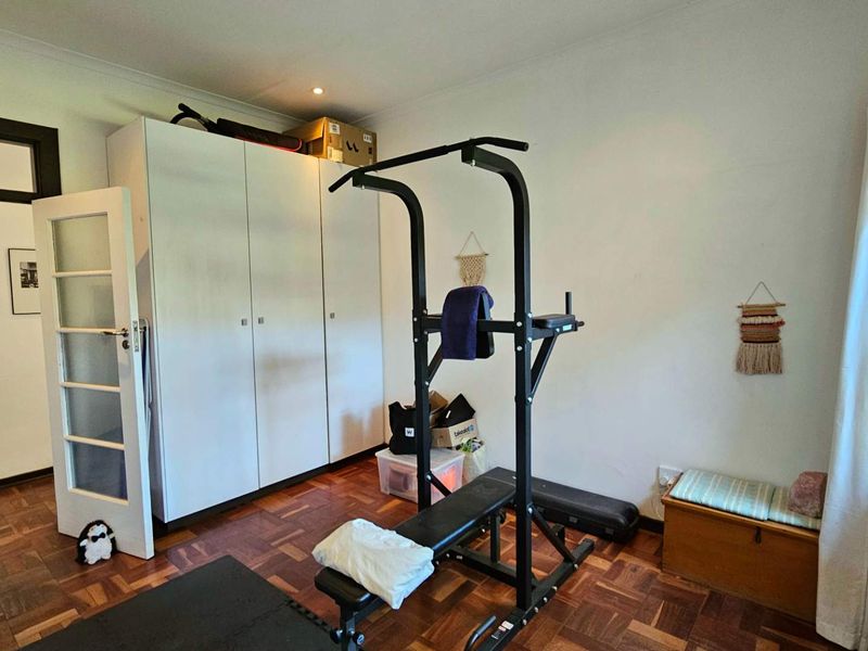 A bedroom featuring classic parquet flooring and built-in storage cupboards, currently utilized as a home gym space.