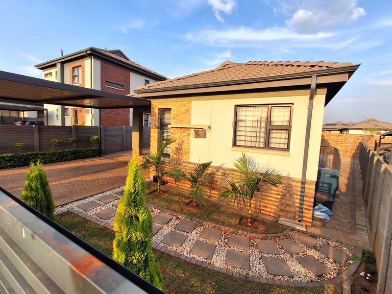 Front view of a modern single-story house featuring a brick and plaster facade, tiled roof, and a paved driveway with an integrated carport.