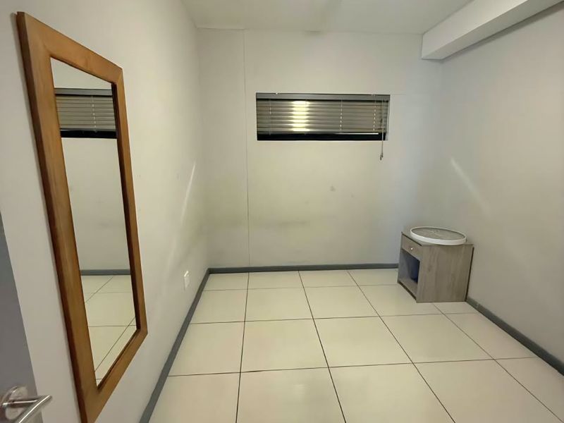 A compact, empty bedroom featuring tiled flooring, a small window with blinds, and neutral wall finishes, ready for personalization.