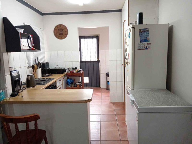 A functional kitchen featuring tiled flooring, built-in cabinetry, a hob, and a security gate leading to the exterior.