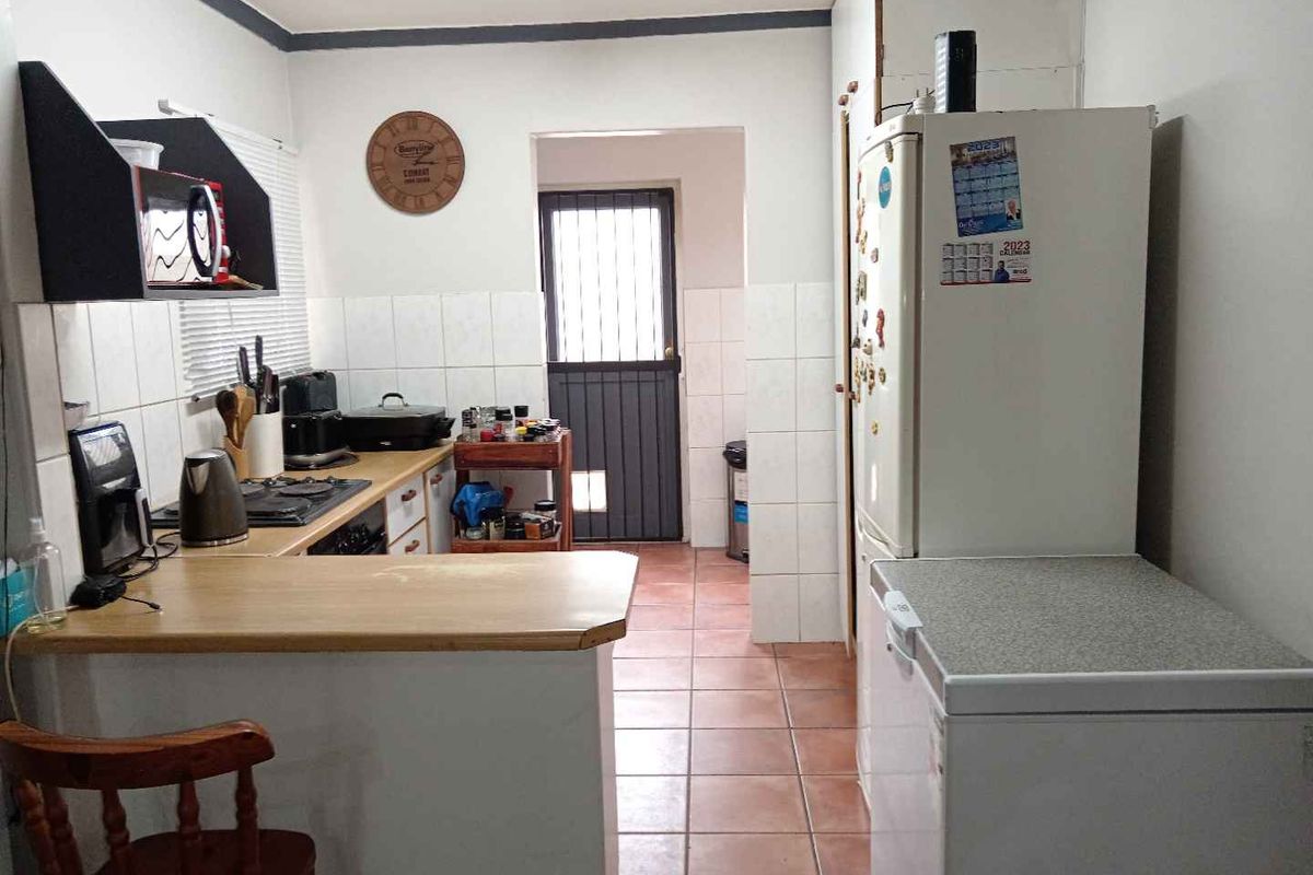 A functional kitchen featuring tiled flooring, built-in cabinetry, a hob, and a security gate leading to the exterior.