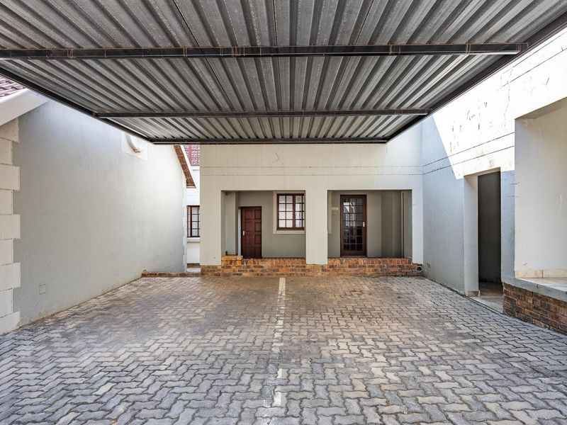 A covered carport area featuring a corrugated metal roof, paved flooring, and brick masonry accents, providing sheltered parking space for the apartment.