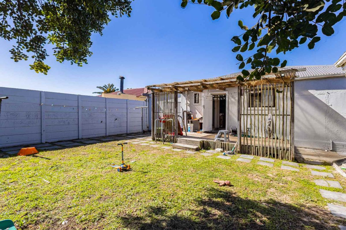 Rear garden featuring a lawn, paved patio area, and a timber pergola structure against the back elevation of the house.