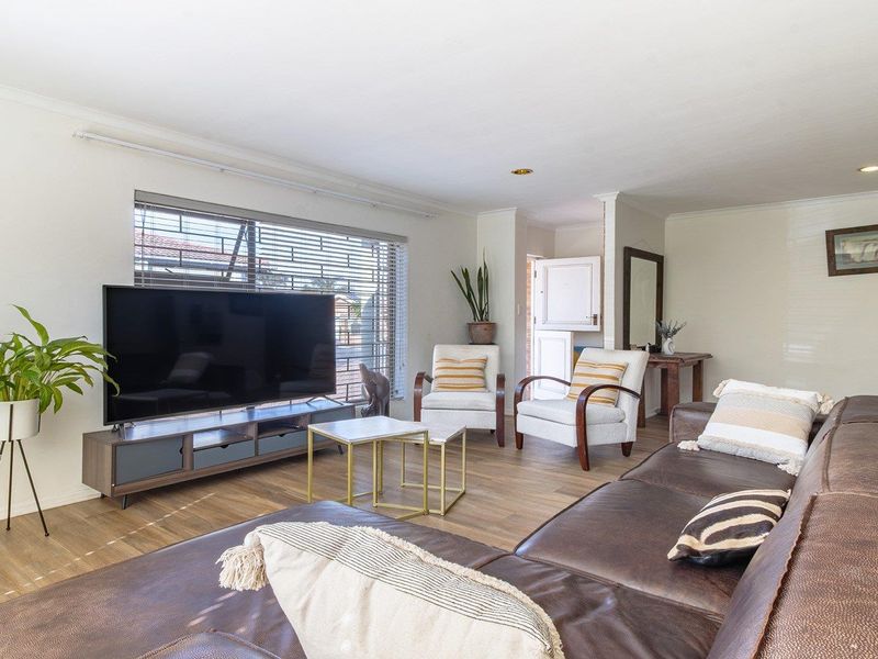 A bright and spacious living room featuring laminate flooring, recessed downlighting, and large windows with venetian blinds.