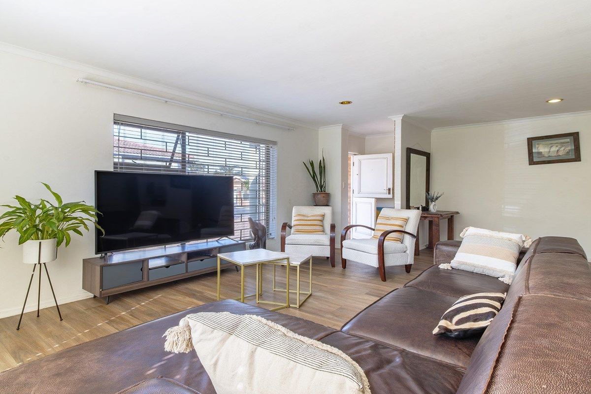A bright and spacious living room featuring laminate flooring, recessed downlighting, and large windows with venetian blinds.