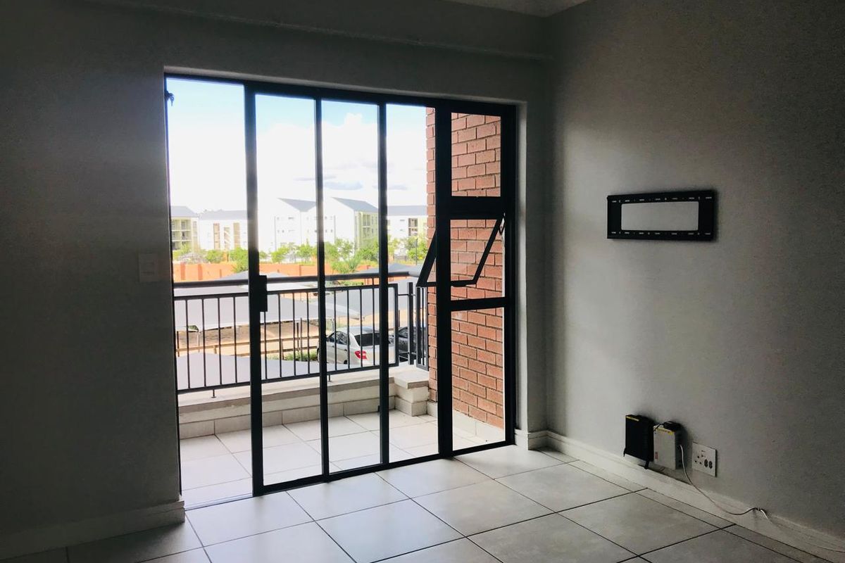 A bright living area featuring tiled flooring and large sliding glass doors that open onto a private balcony.