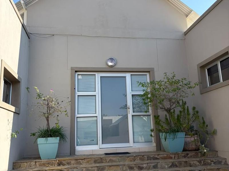 Front entrance featuring stone-clad stairs leading to a modern aluminium-framed glass door under a gabled roof structure.
