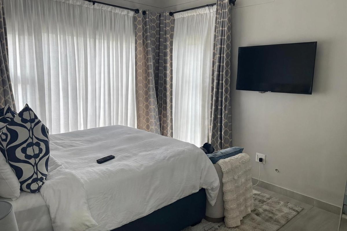 A bedroom featuring tiled flooring, large windows with curtain treatments, and a wall-mounted television.