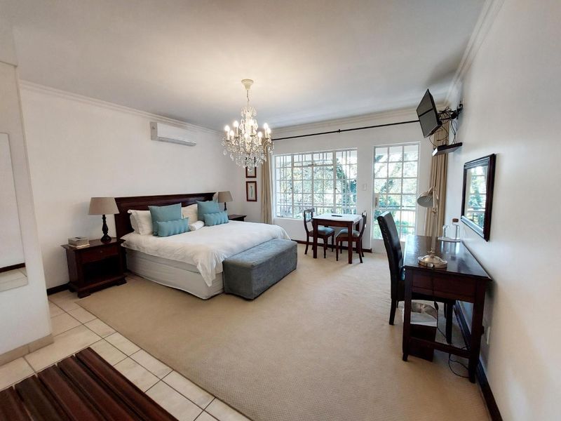 Spacious bedroom featuring neutral carpeting, a split-system air conditioner, elegant chandelier lighting, and direct access to an outdoor area through glass-panel doors.