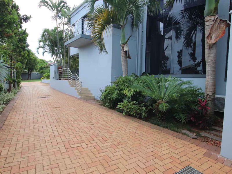 A modern exterior view of the property featuring a paved driveway, a balcony with stainless steel balustrades, and large glass windows.