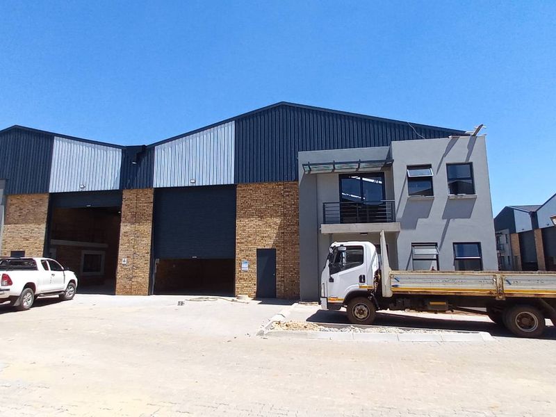 Industrial warehouse complex featuring face brick and metal cladding, large roller shutter doors, and paved exterior yard space.