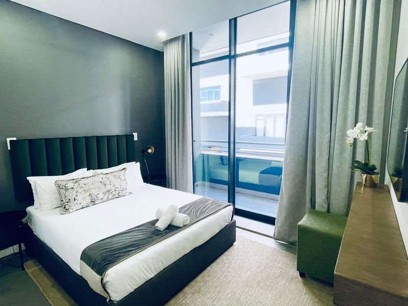 Modern bedroom featuring floor-to-ceiling windows with access to a private balcony, neutral finishes, and contemporary recessed lighting.