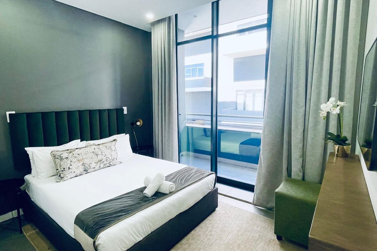Modern bedroom featuring floor-to-ceiling windows with access to a private balcony, neutral finishes, and contemporary recessed lighting.