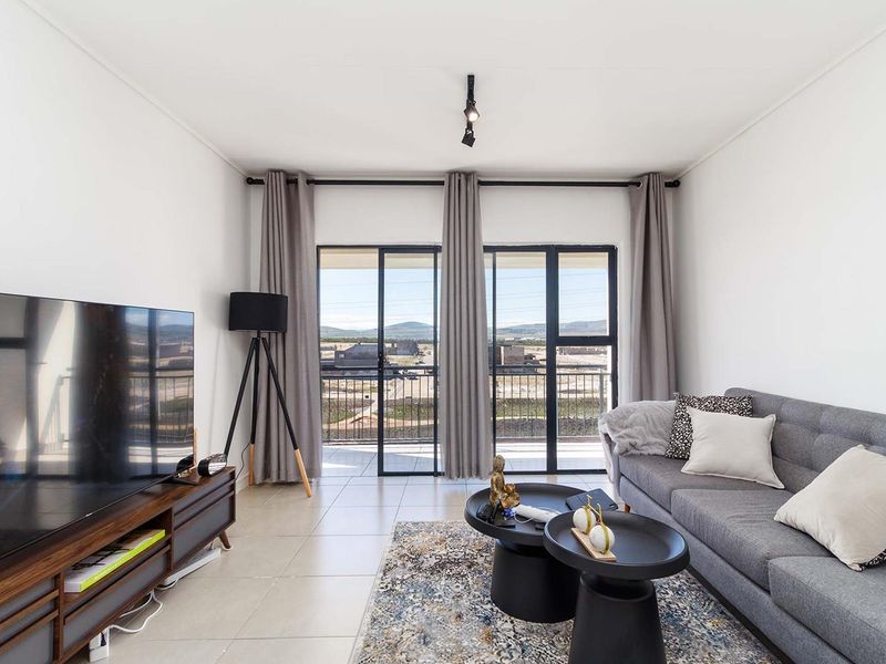 A bright living room featuring tiled flooring, modern track lighting, and large sliding glass doors that provide access to a balcony with scenic views.