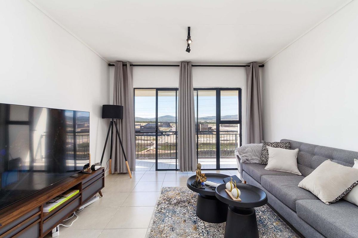 A bright living room featuring tiled flooring, modern track lighting, and large sliding glass doors that provide access to a balcony with scenic views.