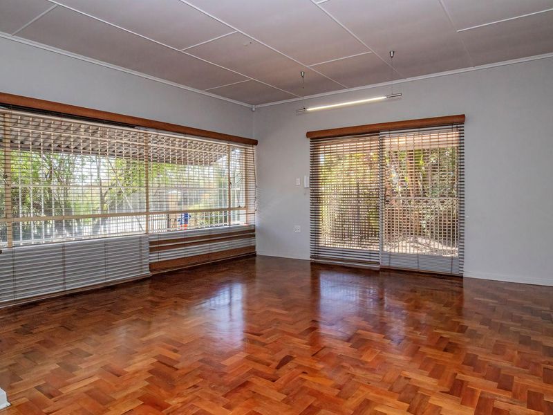 Spacious living room featuring classic parquet flooring, large windows with venetian blinds, and sliding glass doors providing access to the outdoor area.