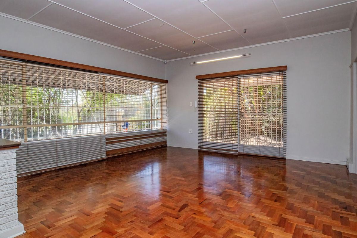 Spacious living room featuring classic parquet flooring, large windows with venetian blinds, and sliding glass doors providing access to the outdoor area.