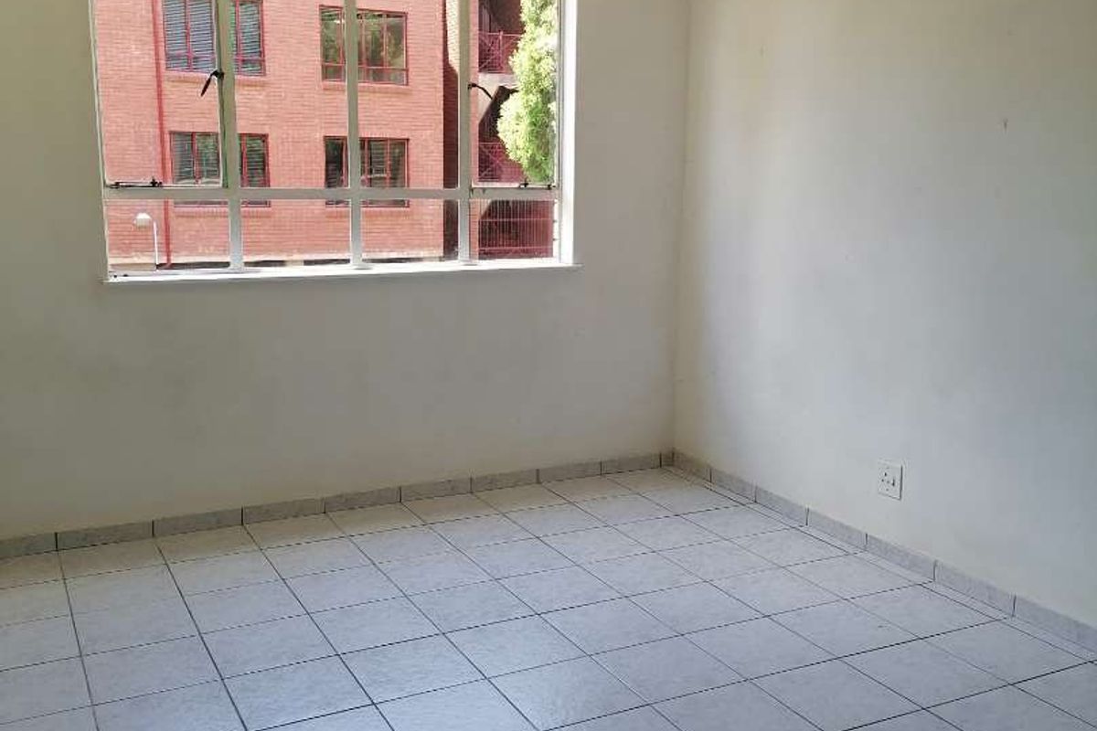 An empty bedroom featuring tiled flooring, a large window providing natural light, and a neutral color palette ready for personalization.