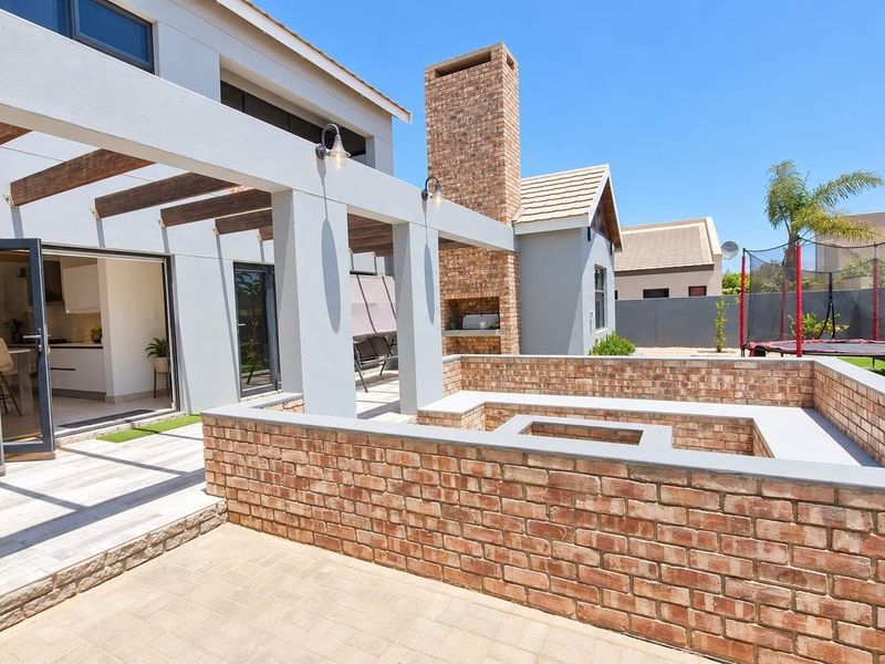 Spacious outdoor patio featuring a built-in brick fireplace, sunken seating area, and a pergola, seamlessly connected to the interior via bi-fold doors.
