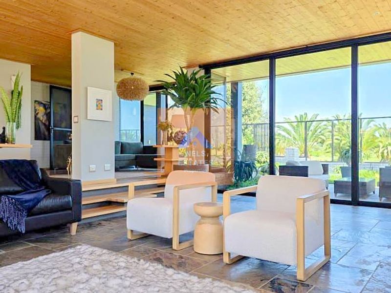 Spacious living area featuring a warm timber-clad ceiling, natural stone flooring, and expansive floor-to-ceiling glass doors providing seamless indoor-outdoor flow.