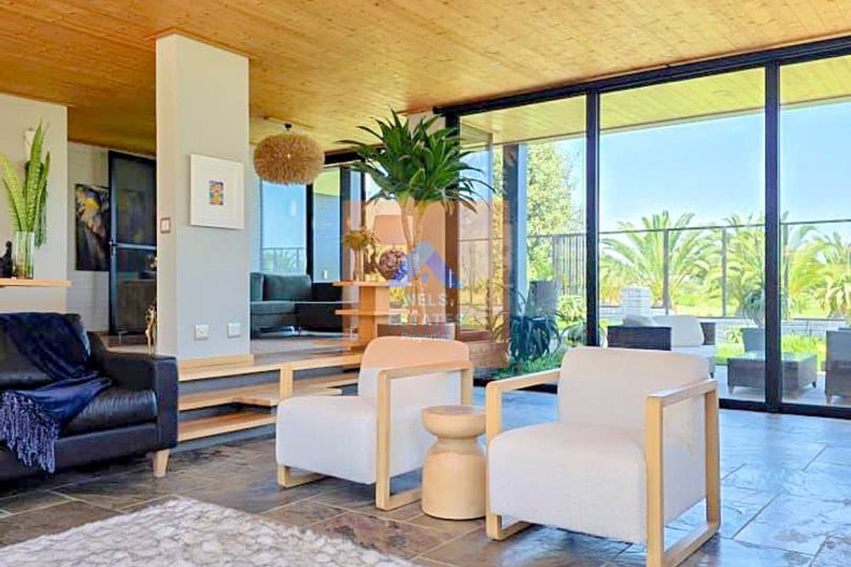Spacious living area featuring a warm timber-clad ceiling, natural stone flooring, and expansive floor-to-ceiling glass doors providing seamless indoor-outdoor flow.