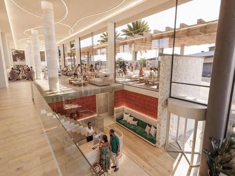 Modern hotel lobby featuring a reception area, stone feature wall, expansive glass windows, and high-end finishes with a seamless transition to outdoor seating.
