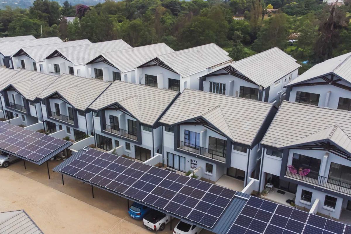 Aerial view of a modern apartment complex featuring multiple units with pitched tiled roofs and extensive solar panel carports.