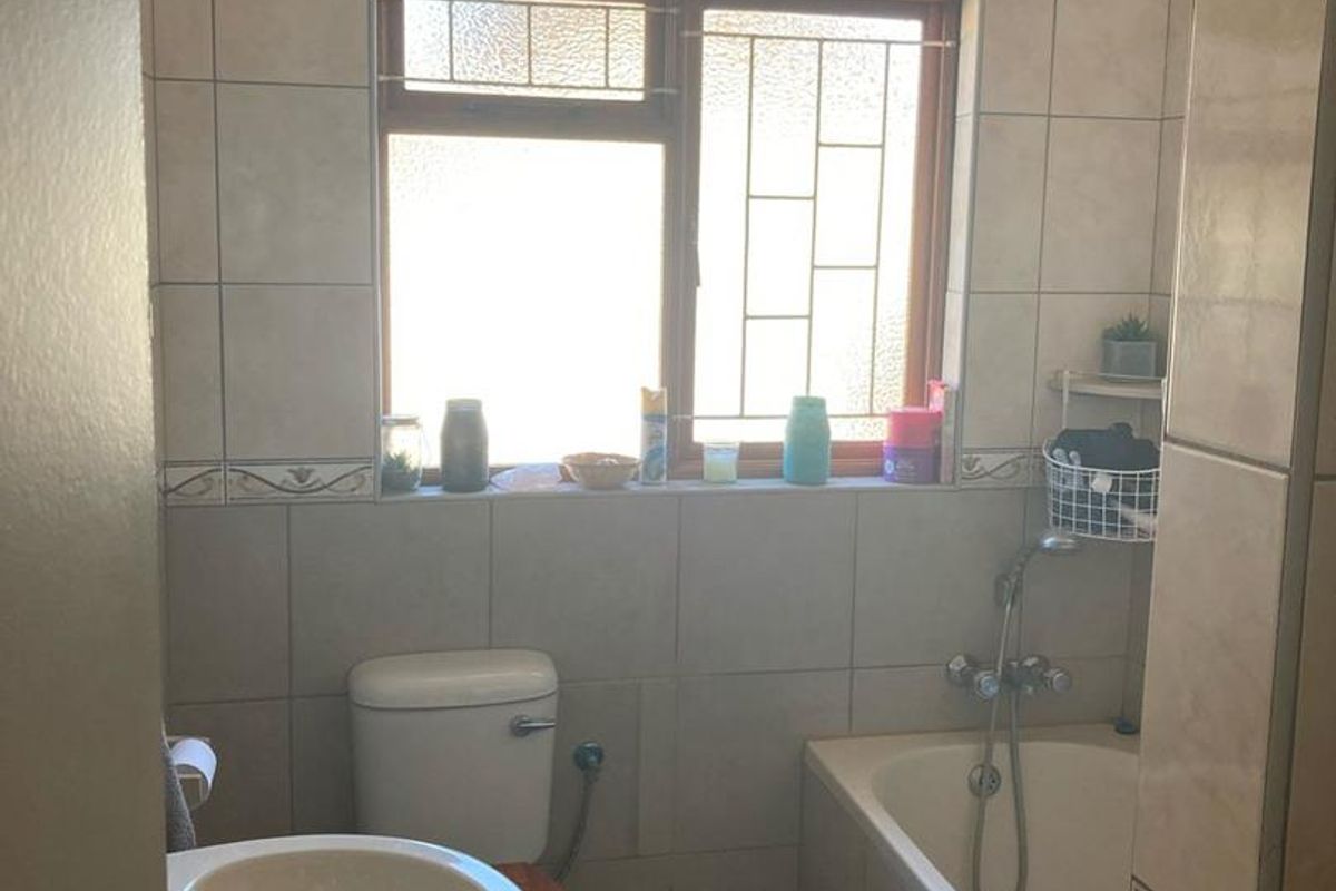 A functional bathroom featuring a pedestal basin, a standard toilet, and a built-in bathtub with wall-mounted shower fixtures and tiled finishes.