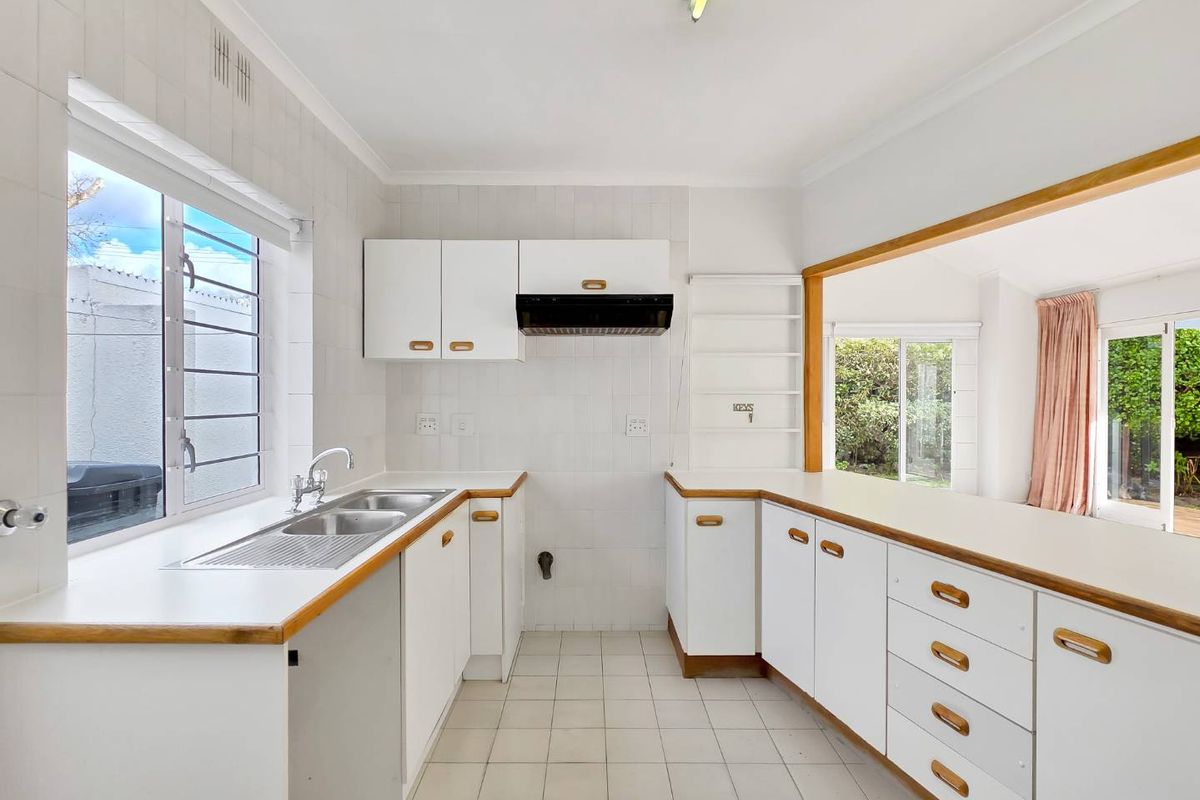 A functional, empty kitchen featuring white cabinetry, laminate countertops, a stainless steel sink, and tiled finishes, offering a clean canvas for modern updates.