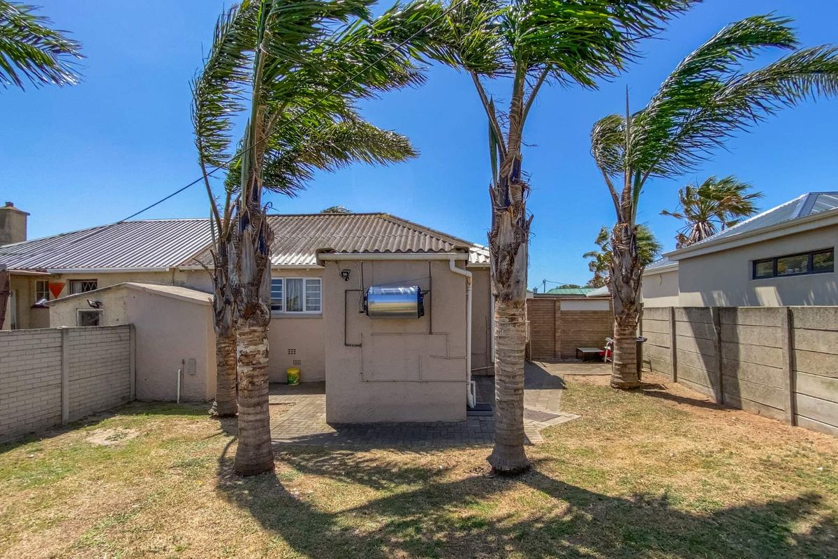 Rear view of the property featuring a paved patio area, exterior solar water heater, and a fenced garden with mature palm trees.