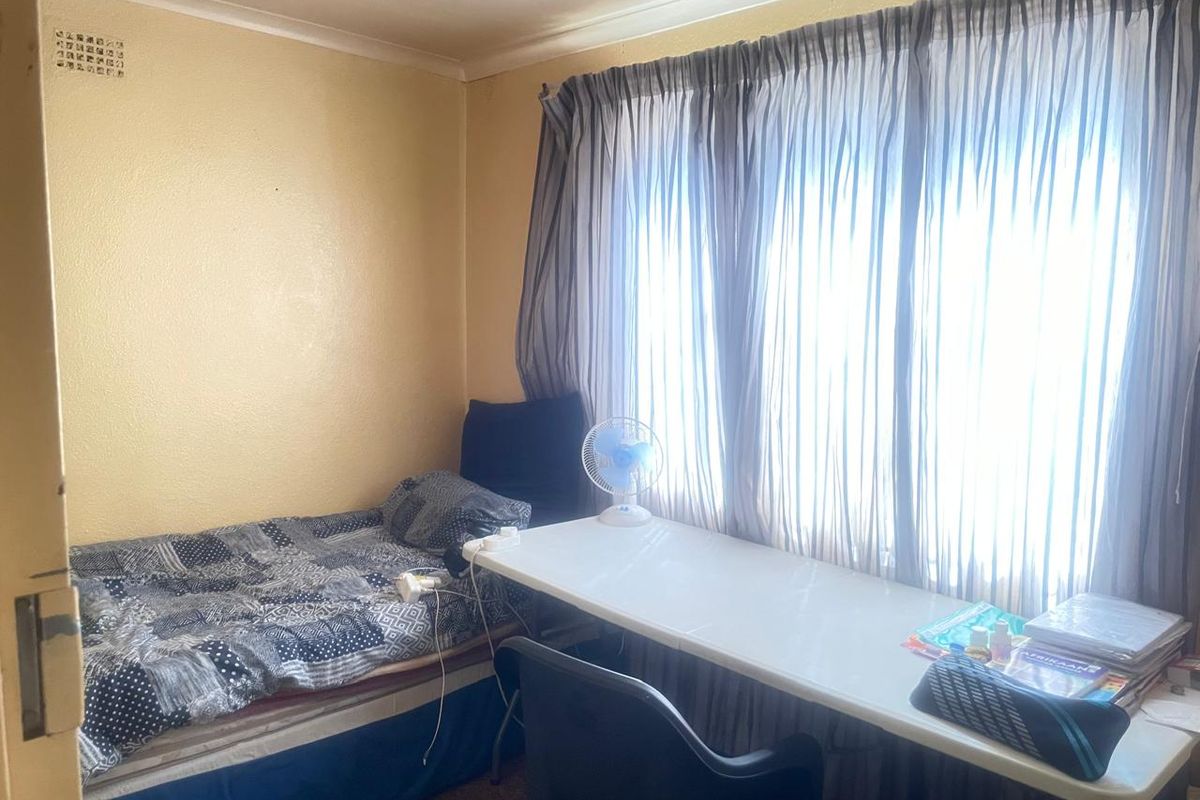 A compact bedroom featuring a window with curtains and a ceiling air vent, requiring cosmetic updates to improve the overall aesthetic.