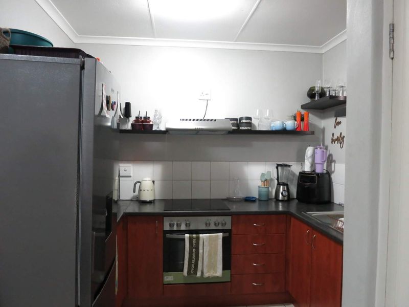 Compact kitchen featuring wooden cabinetry, dark laminate countertops, a built-in oven with electric hob, and a tiled splashback.