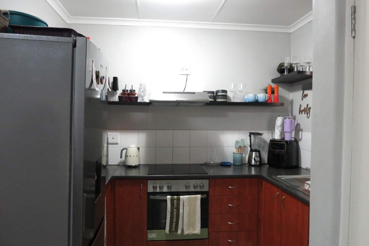 Compact kitchen featuring wooden cabinetry, dark laminate countertops, a built-in oven with electric hob, and a tiled splashback.