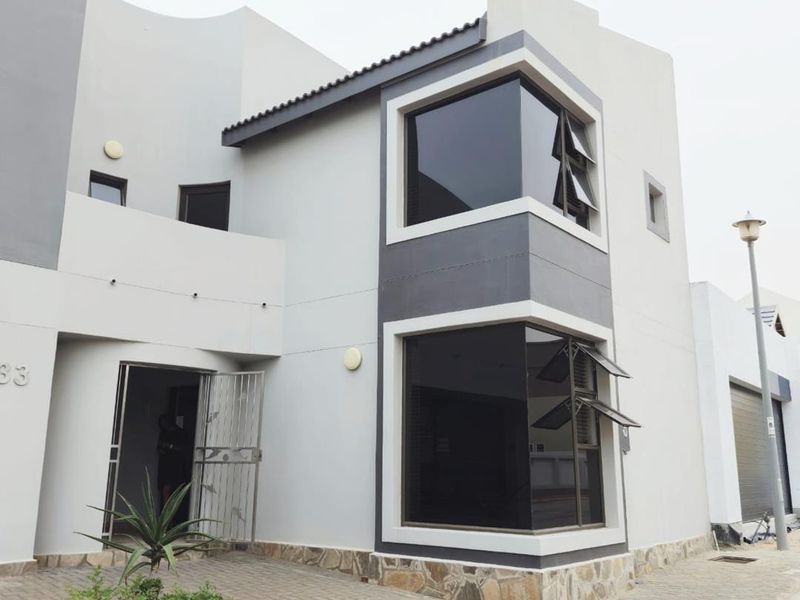 Modern two-story residential facade featuring clean lines, stone cladding accents, corner windows, and a paved entrance area.