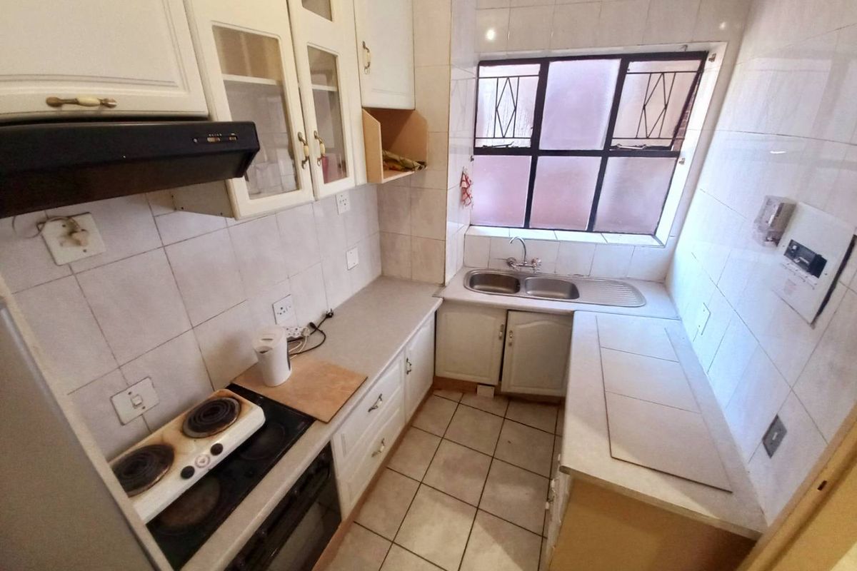 A compact kitchen featuring tiled walls and flooring, built-in cabinetry, a double sink, and a built-in oven with a stovetop.