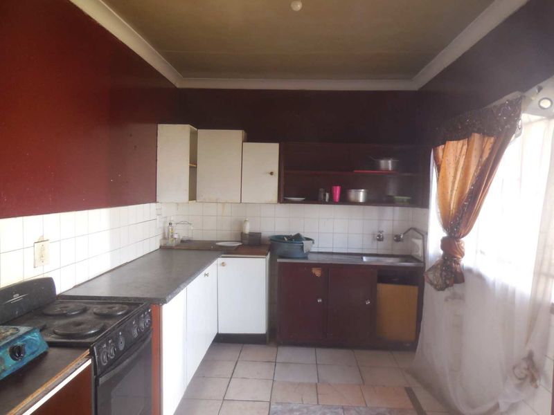 A dated kitchen featuring basic cabinetry, tiled backsplash, and a freestanding stove, offering significant potential for modernization and renovation.