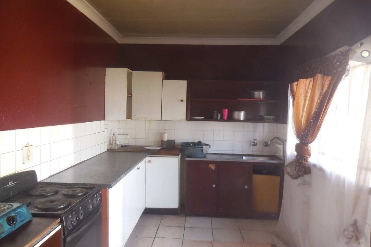 A dated kitchen featuring basic cabinetry, tiled backsplash, and a freestanding stove, offering significant potential for modernization and renovation.