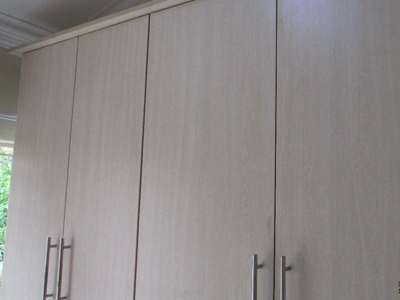 Close-up view of light wood-grain kitchen cabinetry with modern stainless steel handles and decorative crown molding.
