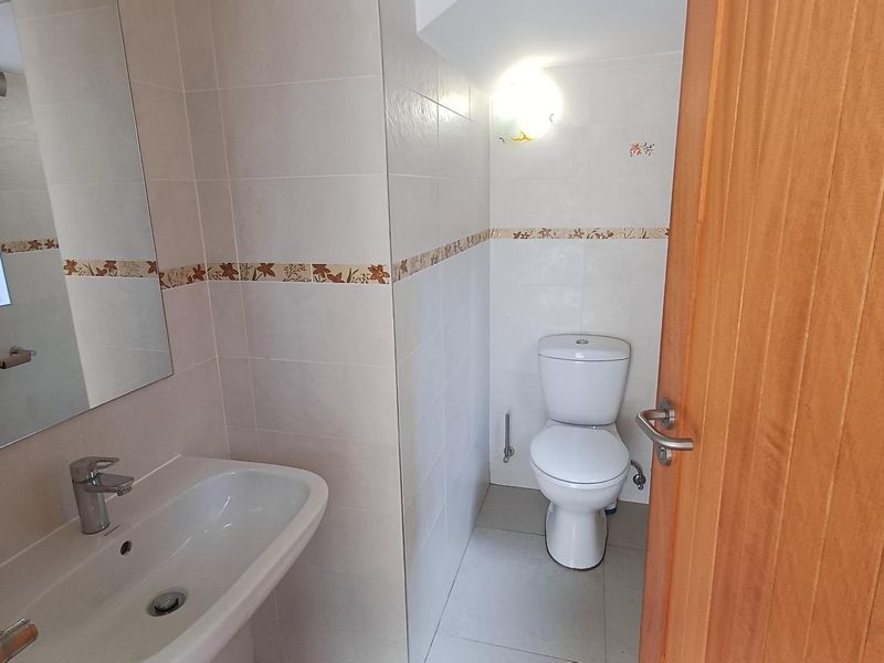 A clean and functional bathroom featuring a pedestal basin, toilet, and neutral wall tiling with a decorative border.