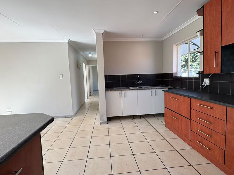 Open plan kitchen area featuring tiled flooring, dark tiled backsplash, and a mix of white and wood-toned built-in cabinetry.