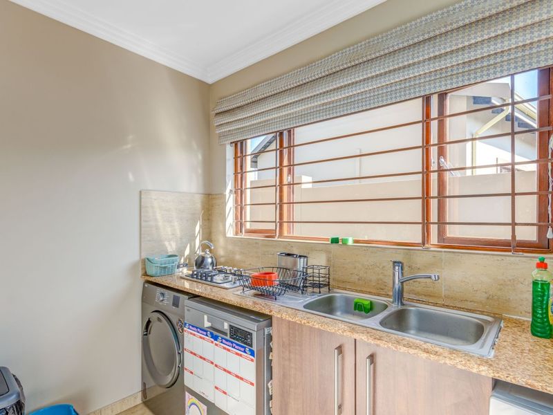 A functional scullery featuring granite countertops, a double basin stainless steel sink, built-in cabinetry, and a gas hob with tiled splashback.
