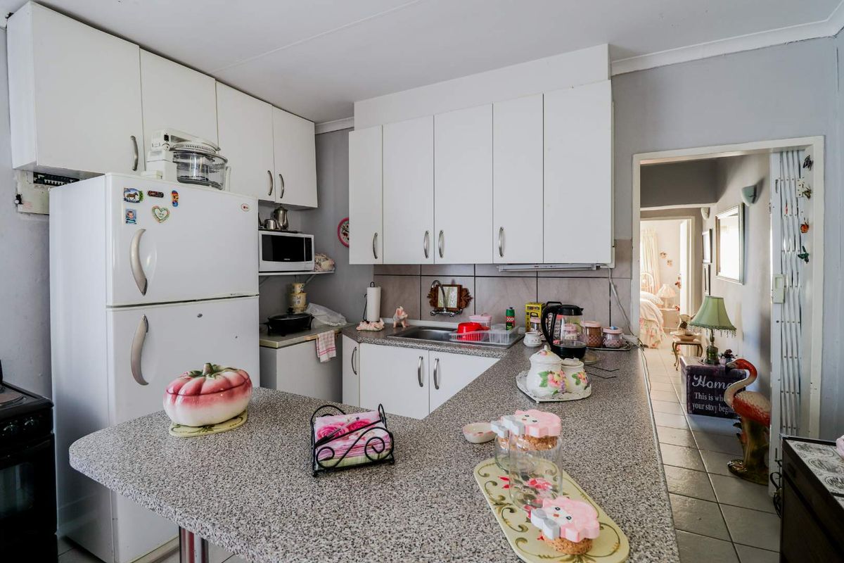 Functional kitchen featuring white cabinetry, granite-look laminate countertops, a stainless steel sink, and a breakfast bar peninsula overlooking the hallway.