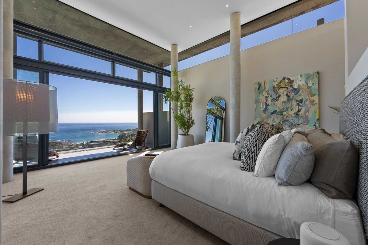 Luxurious bedroom featuring exposed concrete ceilings, floor-to-ceiling sliding glass doors, and expansive ocean views, creating a seamless indoor-outdoor living experience.