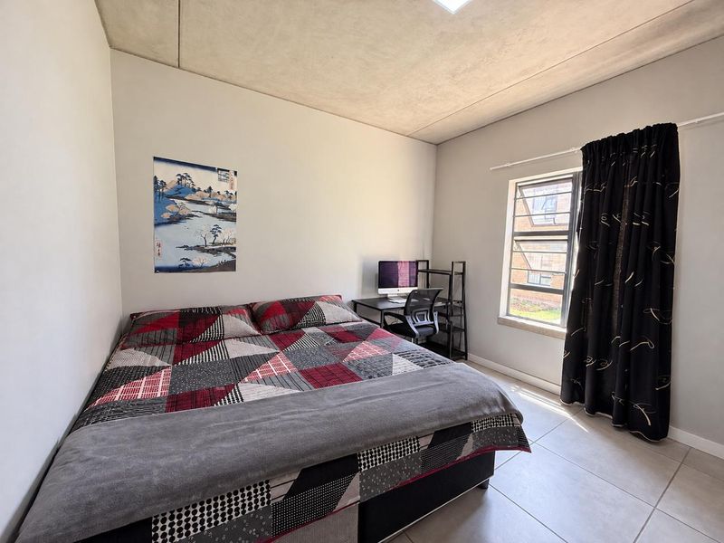 A bedroom featuring tiled flooring and an exposed concrete ceiling, providing a neutral base for interior design.